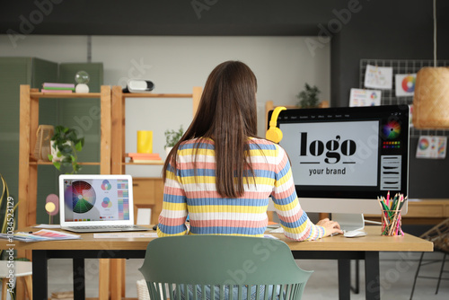 Female graphic designer working at table in office, back view