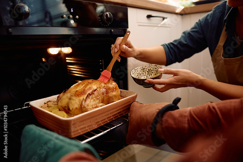 Close up of couple basting roast turkey while making Thanksgiving dinner.