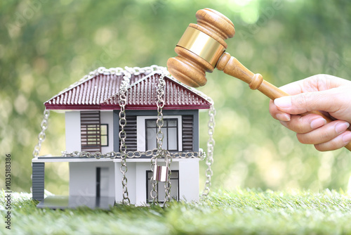 Property auction, Woman hand holding gavel wooden and locked house with padlock and chain on natural green background, lawyer of home real estate and ownership property concept.bankruptcy