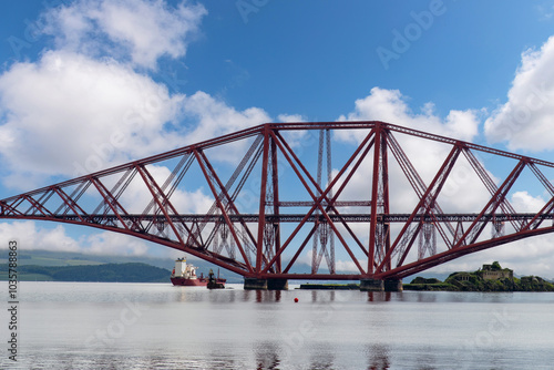 Ship sailing under the red Forth cantilever railway bridge across the Firth of Forth, Queensferry, UK near Edinburgh