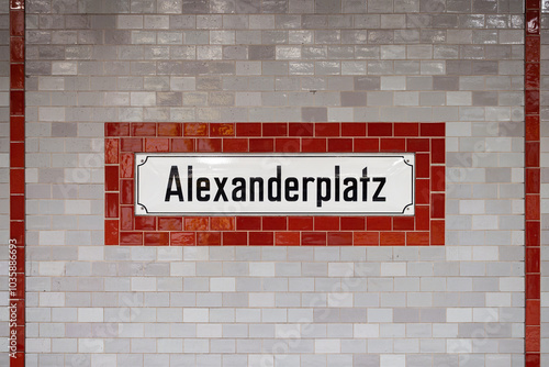 Alexanderplatz sign at the underground train station in Berlin Mitte, Germany. Location name of the public transportation. Red and gray tiled wall with black letters on white.