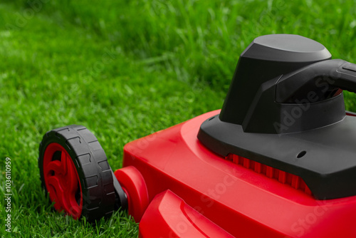 A red and black lawnmower on a green lawn. Mown and unmown grass in the mowing process.