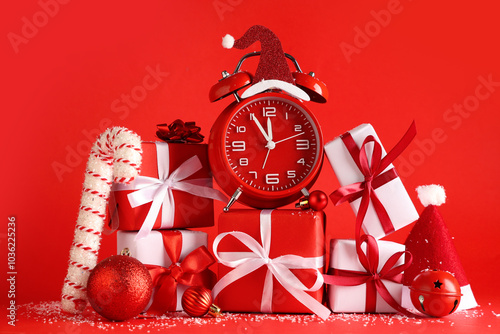 Alarm clock with gift boxes and Christmas decor on red background