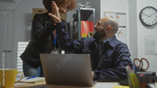 A woman and a man celebrate success with a high-five in a modern police station office, indicating teamwork and job satisfaction.