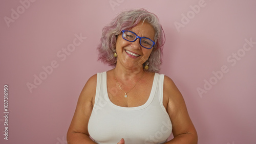 Mature hispanic woman with gray hair and glasses smiling over an isolated pink background