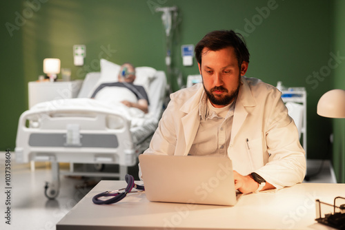 A middle-aged doctor sits tiredly at his desk in a hospital room. An overtired doctor at work