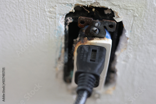 A close-up of a burnt electrical outlet with a plug still inserted, showing signs of damage from an electrical fire caused by faulty wiring. 