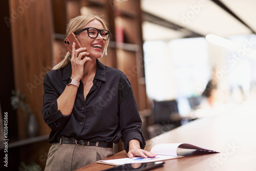 A happy, professional woman talks on the phone in a modern office, showing her business success