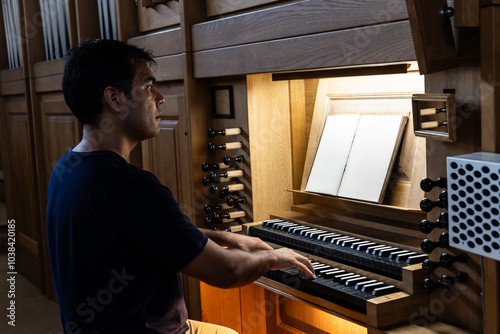 Right side view of organist sitting at organ with blank musical score playing organ in Catholic Church.