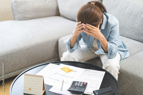 Debt and financial concept, stressed asian young woman have a headache while sitting on sofa calculate expenses, income, looking bills of credit card for prepare payment or pay bills on table at home.