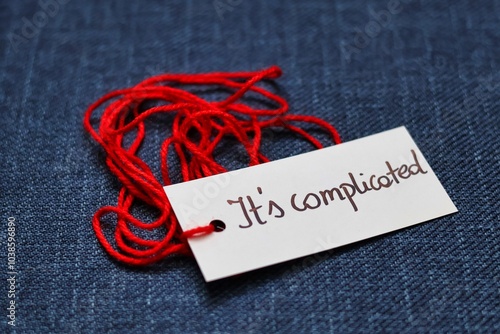 A photo illustrating the saying that it's complicated; Red thread with the handwritten inscription 'it's complicated' on a navy blue background