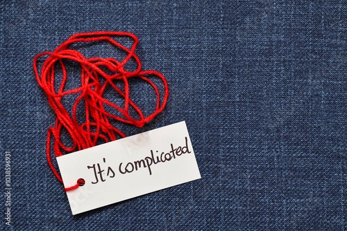 A photo illustrating the saying that it's complicated; Red thread with the handwritten inscription 'it's complicated' on a navy blue background