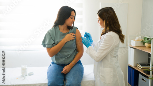 Latin female patient is getting vaccinated by a doctor wearing gloves in a medical office