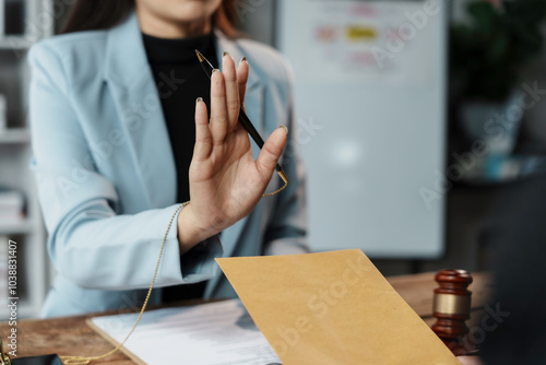 Businesswoman is refusing to sign documents by raising her hand with pen at office desk with gavel