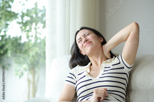 Stressed asian woman suffering neck ache on uncomfortable couch