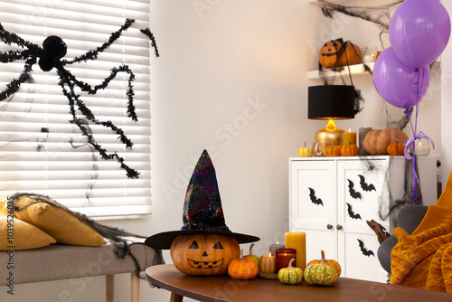 Burning candles and pumpkins on table in room decorated for Halloween