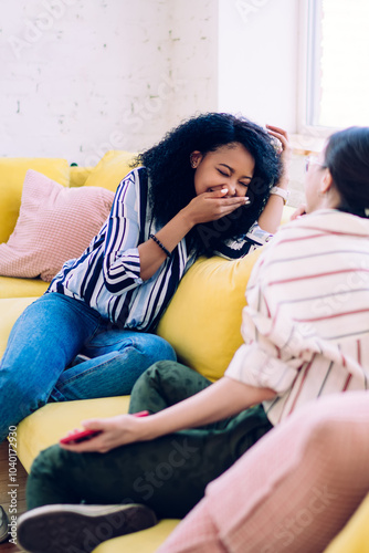 Close female friends gossiping on yellow sofa