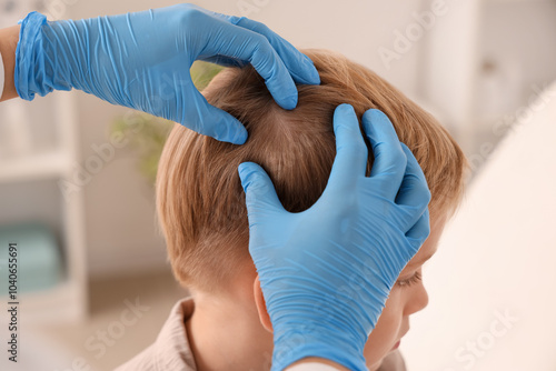 Female doctor checking little boy's head for pediculosis in clinic, closeup