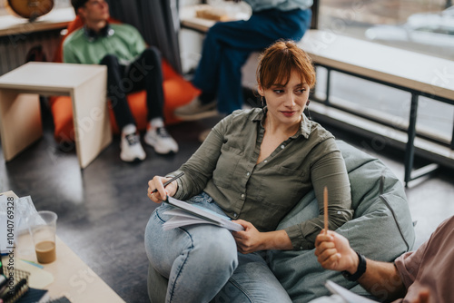 Students interact in a relaxed, collaborative environment, emphasizing learning and discussion. The setting is informal, with bean bags and natural light, enhancing the educational experience.