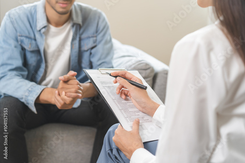 Psychology, depression. Happy smile asian young man patient mental therapy explain symptom with psychologist while doctor woman taking notes at clinic. Psychologist with sick mental health person.