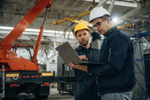 Architect is showing the plan on the laptop. Two male factory workers are in the warehouse