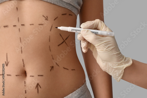 Plastic surgeon marking woman's belly on light background, closeup