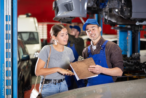 Positive young auto-mechanic communicating with glad woman client of car workshop about service fees indicated on sheets