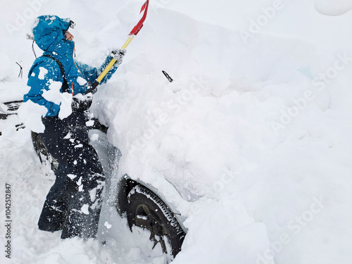 Traveling to the mountains in winter: woman clears snow from her vehicle, which is totally trapped, with a shovel; Mendoza, Argentina.