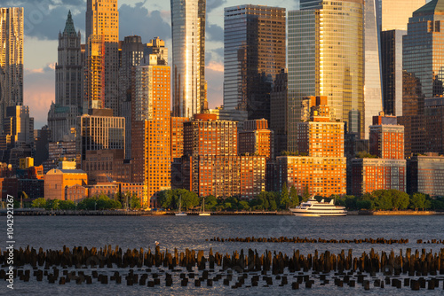 Golden sunset light on Lower Manhattan skyline. Financial District skyscrapers and boats cruising on Hudson River, New York City