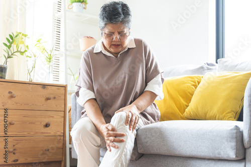 Body arthritis muscles stiff problem, aged woman suffering on leg, pain knee from disease chronic, hand massage rubbing joint injury, mature hurt or sore sitting on sofa at home. Health care people.