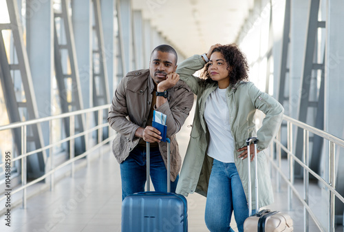 Upset African American Tourists Couple missed the flight or train, both standing next to a bright suitcase at a modern transit station. High quality photo