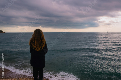 Mujer joven que se siente sola y triste o pensativa o esperando. mirando el mar en un día sombrío , Young woman feeling alone and sad or thoughtful or waiting. looking at the sea on a gloomy day