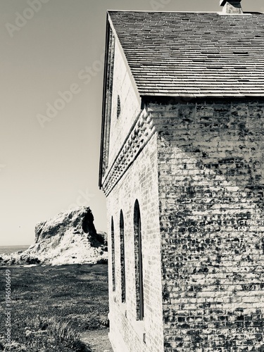 A black and white capture of a former foghorn station's architectural details, with its distinctive arched windows and weathered brick walls set against a coastal sea stack.