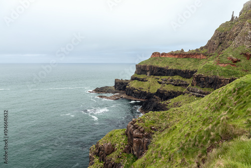 Coastal cliffs at Giant Causeway on a cloudy day. The ocean merges with the sky, while the textured cliffs and bright green grass contrast against the soft light