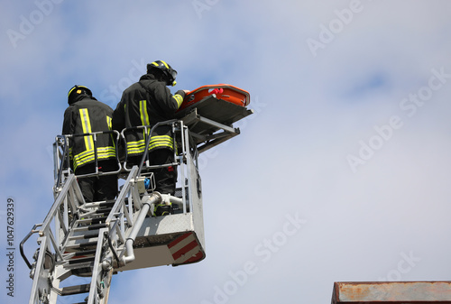 two Firefighters on the basket of the ladder truck during the intervention to recover the injured man with the stretcher