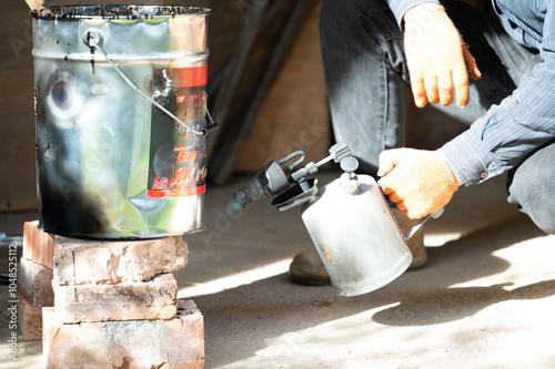 A man uses a kerosene lamp to heat resin in a bucket, working with waterproofing and resin.