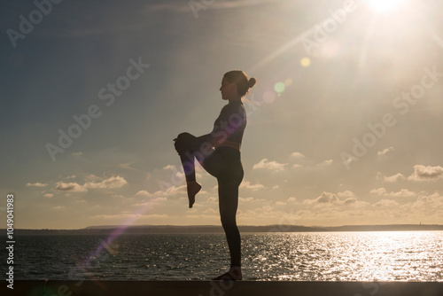 Silhoutte of a sporty woman doing a leg stretch outdoors by the sea