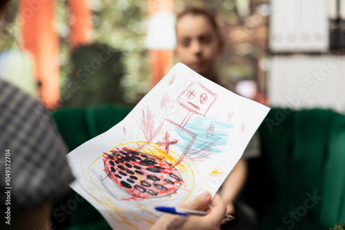 Therapist studies ominous gory drawings from a troubled teen, doing a psychoanalysis at therapy session. The dark sketches depict disturbing violent behavior, unsettling danger signs. Close up.