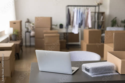 Notebook laptop unpacked first on table with belongings in boxes at new store area at moving day. Starting own dropshipping or transportation business at new rented leased room for storage and office