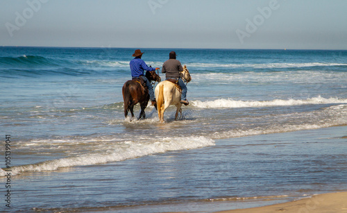 Two men riding horses on the beach at the waters edge. The image was made in Rosarito Mexico