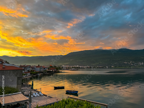 Breathtaking sunset over Lake Ohrid, North Macedonia. Sky is ablaze with vibrant colors of orange, pink, and purple reflecting on calm waters. Silhouette of small town nestled against the mountainside