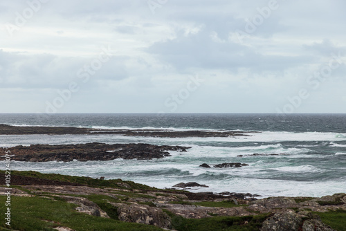 A rocky shoreline meets the restless Atlantic Ocean waves under a cloudy sky, capturing the wild and rugged coast of Ireland