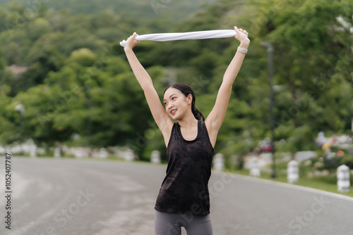 Post-Workout Bliss: A young woman runner celebrates her fitness journey, arms raised in triumph, holding a towel, against a lush green mountain backdrop. The image radiates health, vitality.