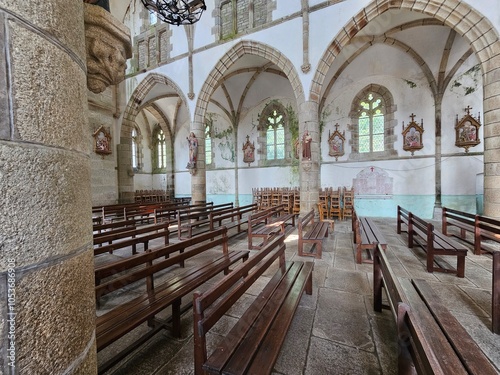 Des rangées de bancs en bois remplissent l'intérieur de l'église, entourées par des murs en pierre ornés de statues et de stations du chemin de croix, avec de grandes arches et des vitraux