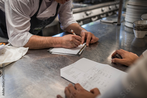 Professional chefs collaborate in a busy kitchen, writing notes and planning. A glimpse into teamwork, culinary preparation, and kitchen management in a dynamic cooking environment.