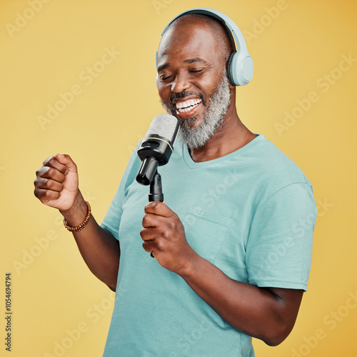 Black man, headphones and mic in studio, singing song and streaming sound on yellow background. Mature person, energy and subscribe to music for karaoke, technology and online for hip hop playlist