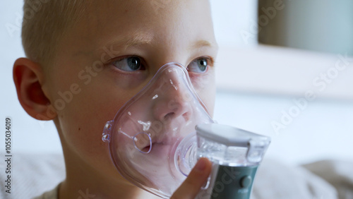 A young boy sits quietly at home, using an inhaler for treatment. This is a common method for managing asthma and preventing respiratory illnesses like colds.