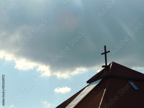 The tiled roof of a Protestant church with a cross on top against a blue sky with a large gray cloud in the background