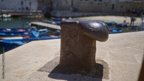 Close-up of a metal bollard on a sunny day in monopoli, italy, with colorful boats docked in the background.