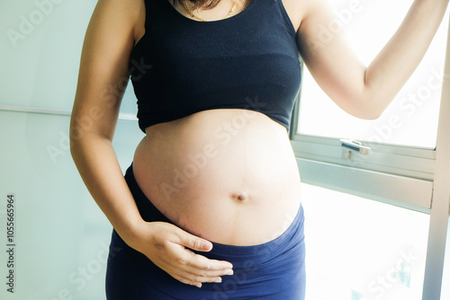 Pregnant asian women standing with window light shw belly